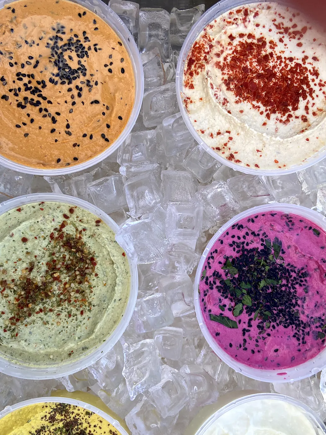 Garnished tubs of hummus on ice at the market