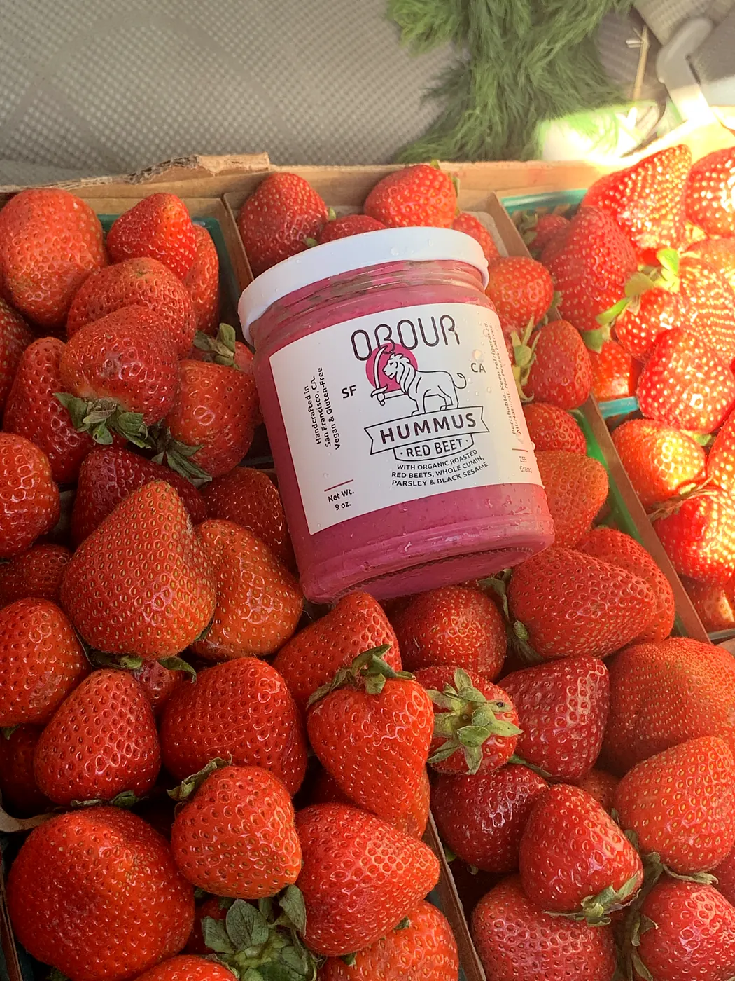 A jar of Red Beet hummus on a crate of strawberries