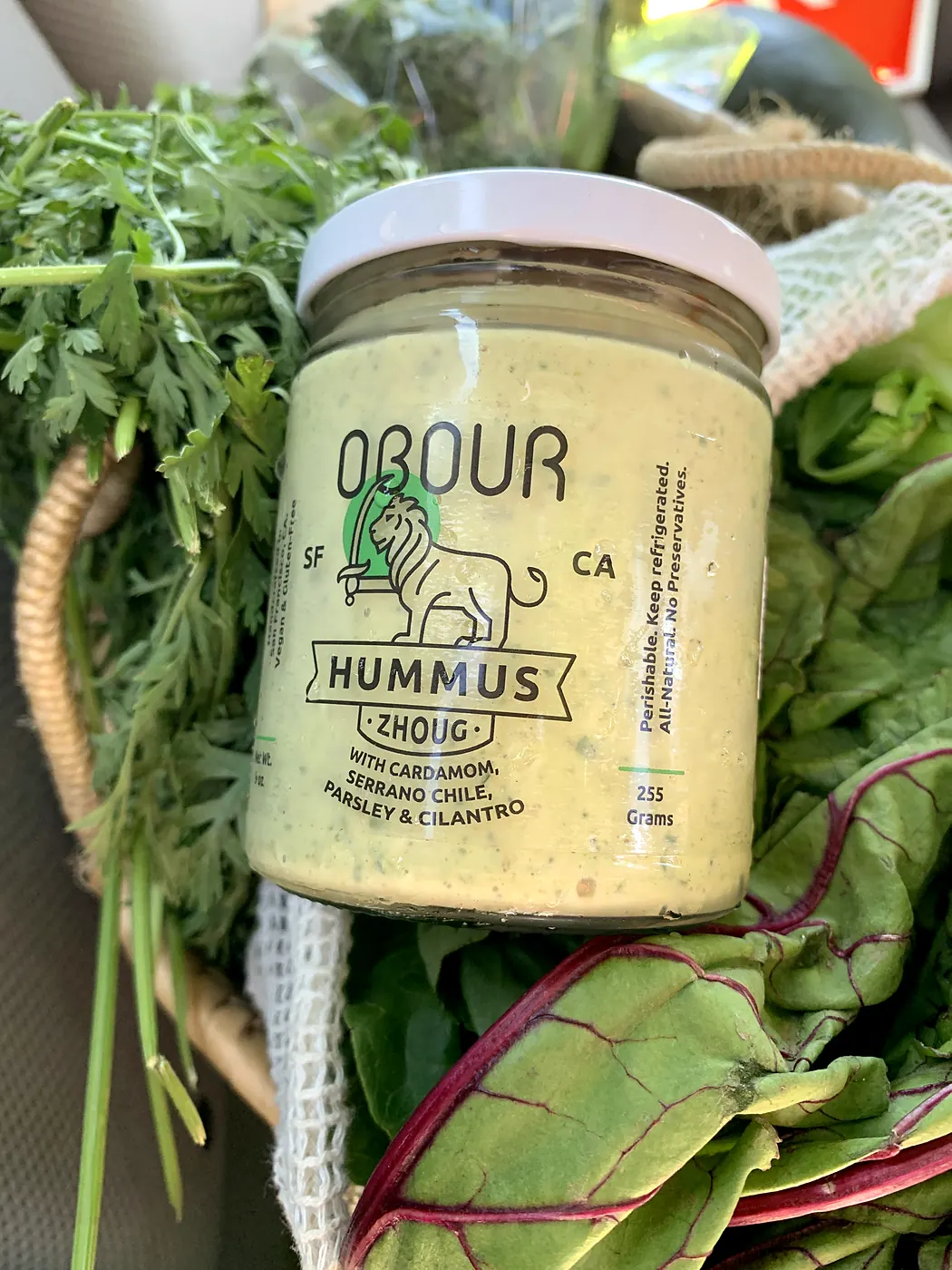 A jar of Zhoug hummus in a market basket of greens